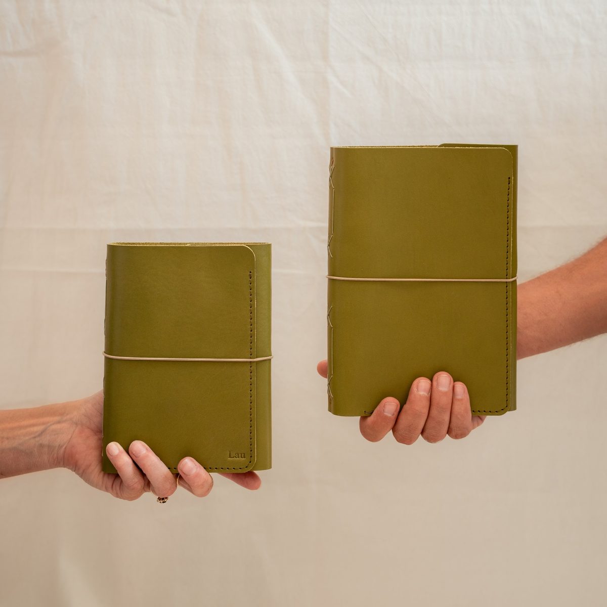 Deux carnets cuir vert L'Carnet Édition tendus à bout de bras, l'un embossé « Lau »